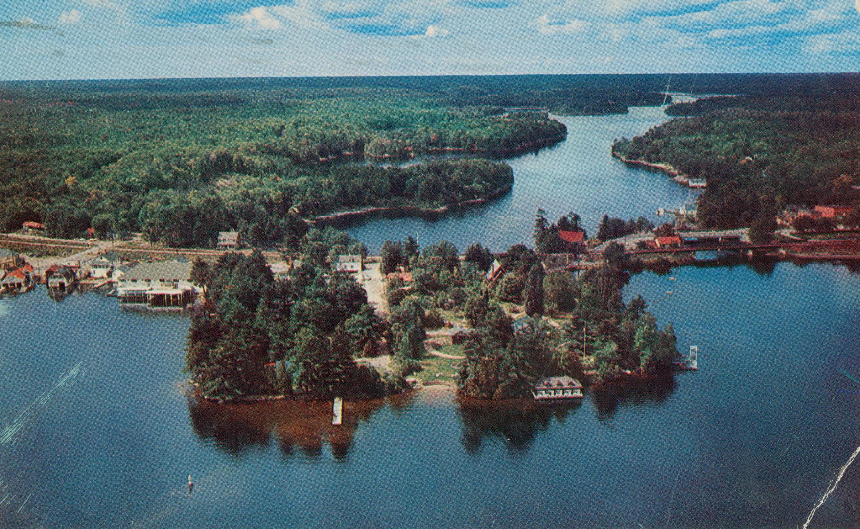 Color aerial shot of a lake with a small cottage community on land in the middle of it.