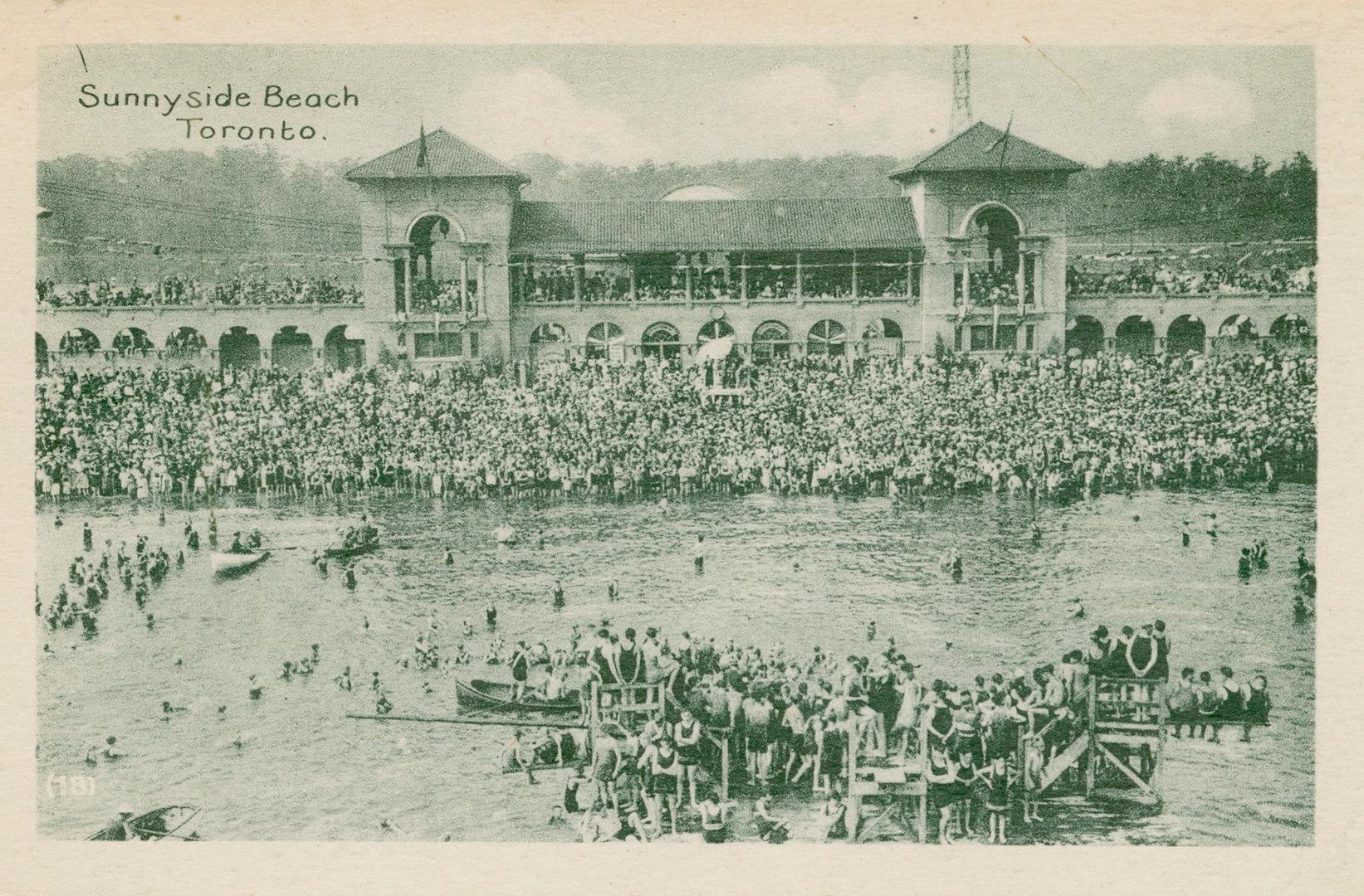 Picture of a crowded beach and lake with a building in the background. 