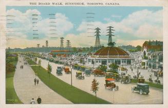 Picture of a boardwalk, road with cars driving and parked and large amusement park. 