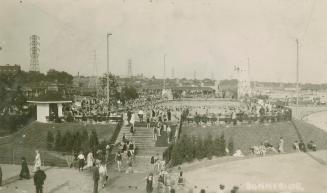 Picture of a large swimming pool crowded with people with beach in foreground. 