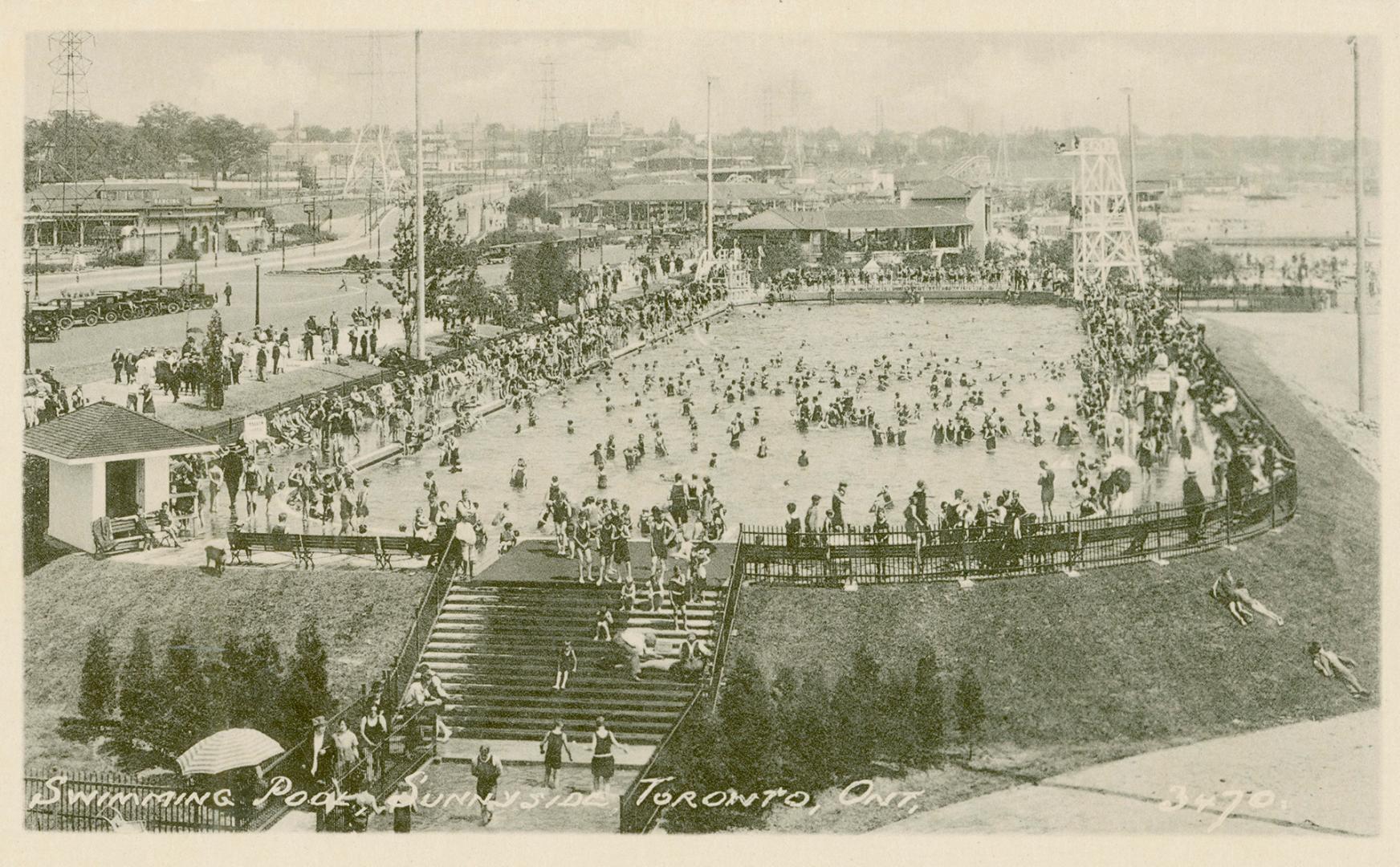 Distant view of large swimming pool and crowds of swimmers with beach and stairs to pool in for…