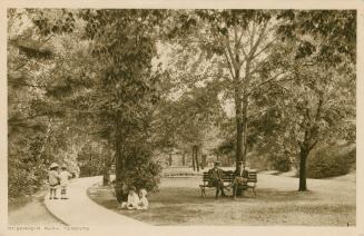 Black and white picture of people sitting on a bench and walking on a wooden path in a wooded p…