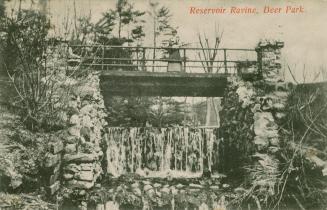 Black and white picture of a woman looking over the railing of a bridge spanning a waterfall.