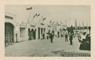 Black and white picture of people standing on a boardwalk in front of a row of arcade entrances…