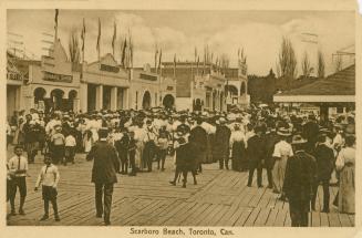 A crowd of people walk around buildings at an amusement park. 