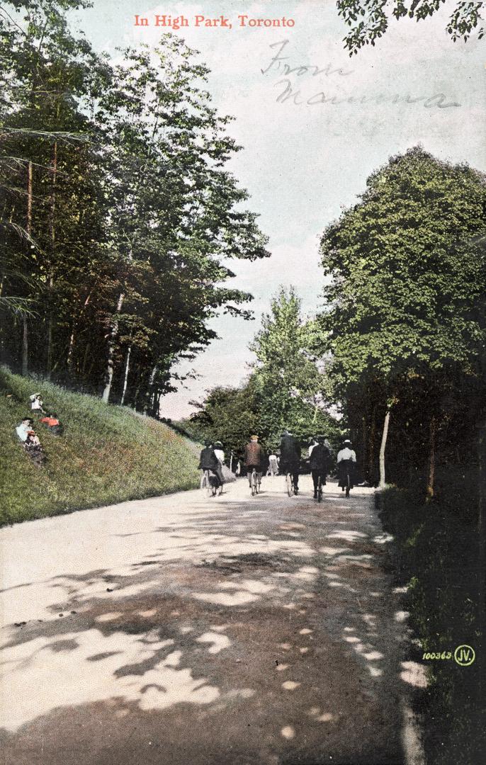 People cycling on a path in a park while others look on.