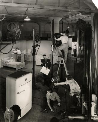 A photograph of a studio area with a high ceiling and lighting rigs illuminating a set with a r…