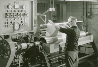 A photograph of a man wearing glasses pulling a large sheet of paper from intaglio cylinders du…