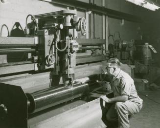 A photograph of a man with one hand on a rotary press during the process of printing Simpsons-S…