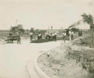 A photograph of a road being paved, with several workers shoveling tar onto the roadway.