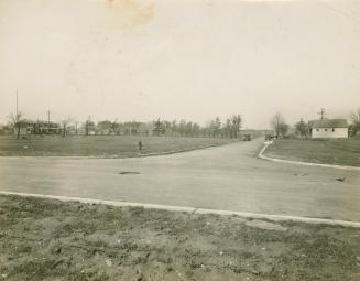 A photograph of a suburban neighbourhood, with grassy fields, trees and a few houses visible on…