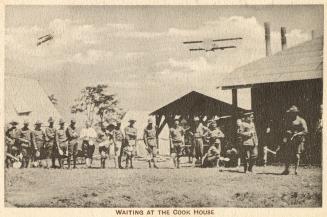 Sepia toned picture of a group of airmen outside buildings in a military camp. Planes are flyin…