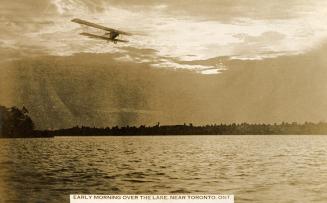 Black and white shot of an air plane flying across a body of water.