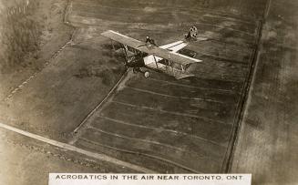 Black and white shot of an air plane flying across a field with a man performing stunts on the …