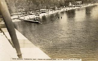 Black and white aerial shot of people swimming and sunbathing on a beach.