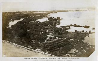 Aerial shot of houses and structures on land beside a lake. B & W.