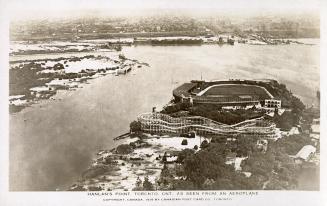 Aerial shot of an amusement park on land beside a lake. B & W.