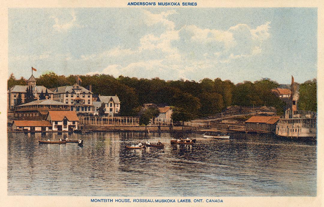 People in canoes on a lake in front of buildings of a grand hotel complex.