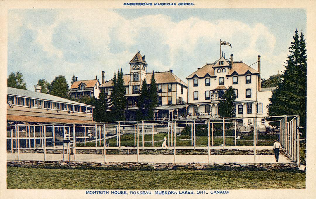 A tennis court in front of three large cottage buildings.