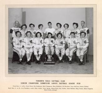 A photograph of a women's softball team posing in front of a trophy. They are sitting and stand ...