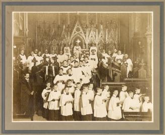 A photograph of a church choir comprised of adult men and boys, wearing robes and standing in f…