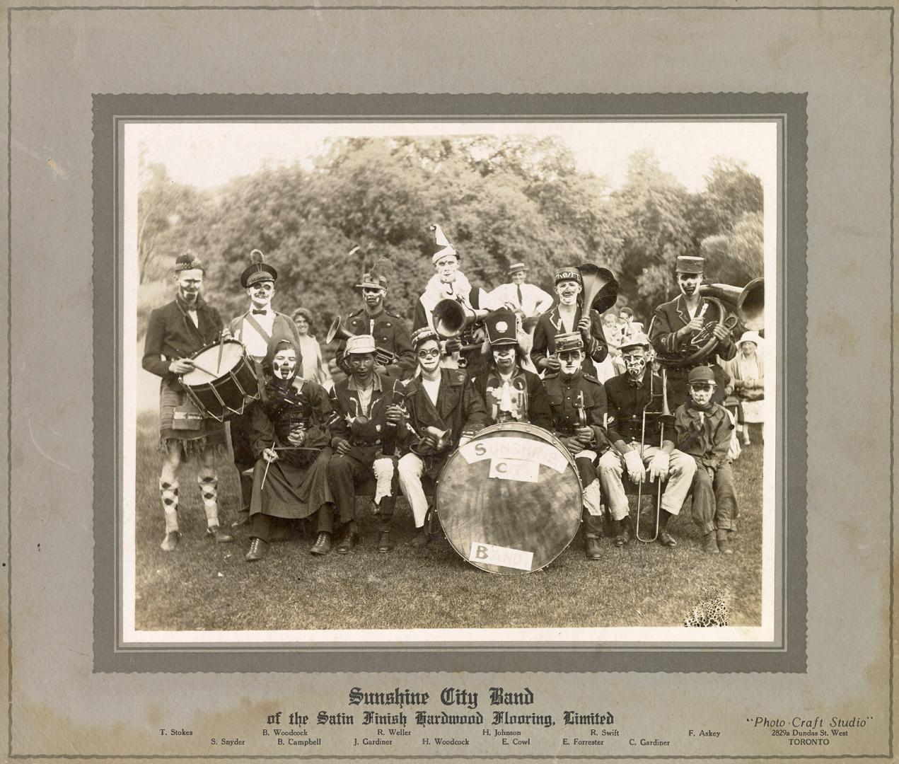 A photograph of the members of a band posing on a grassy lawn in front of some trees and bushes ...