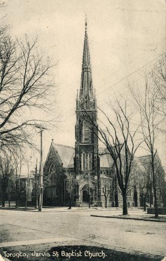 Picture of large stone church on street corner with prominent steeple and trees surrounding it.…