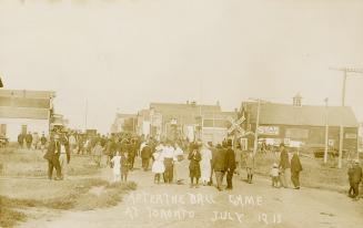 Black and white photograph of a crowd of people walking along a street after watching a basebal ...