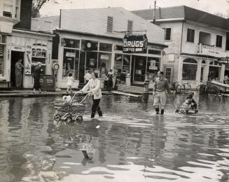 Picture of a woman pushing baby carriage and man pulling wagon with two children wading through…