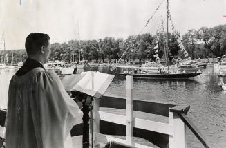 Picture of minister standing on dock blessing several boats in a lagoon. 