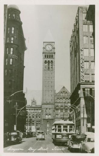 Black and white photograph of a busy city street with a large public building with a clock towe…