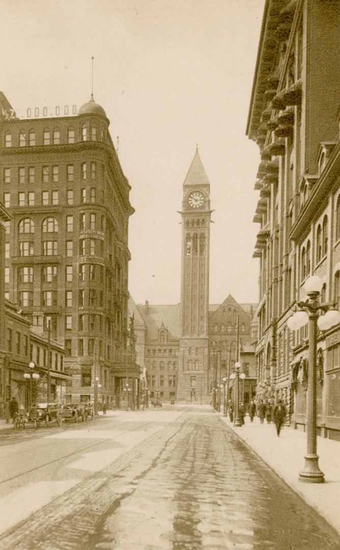 Sepia toned photograph of a busy city street with a large public building with a clock tower at…