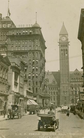 Black and white photograph of a busy city street with a large public building with a clock towe…