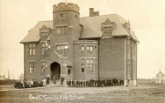 Black and white photograph of a large crowd standing in front of a huge collegiate building.