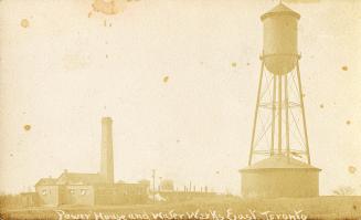 Black and white photograph of a large, water tower in front of an industrial building.