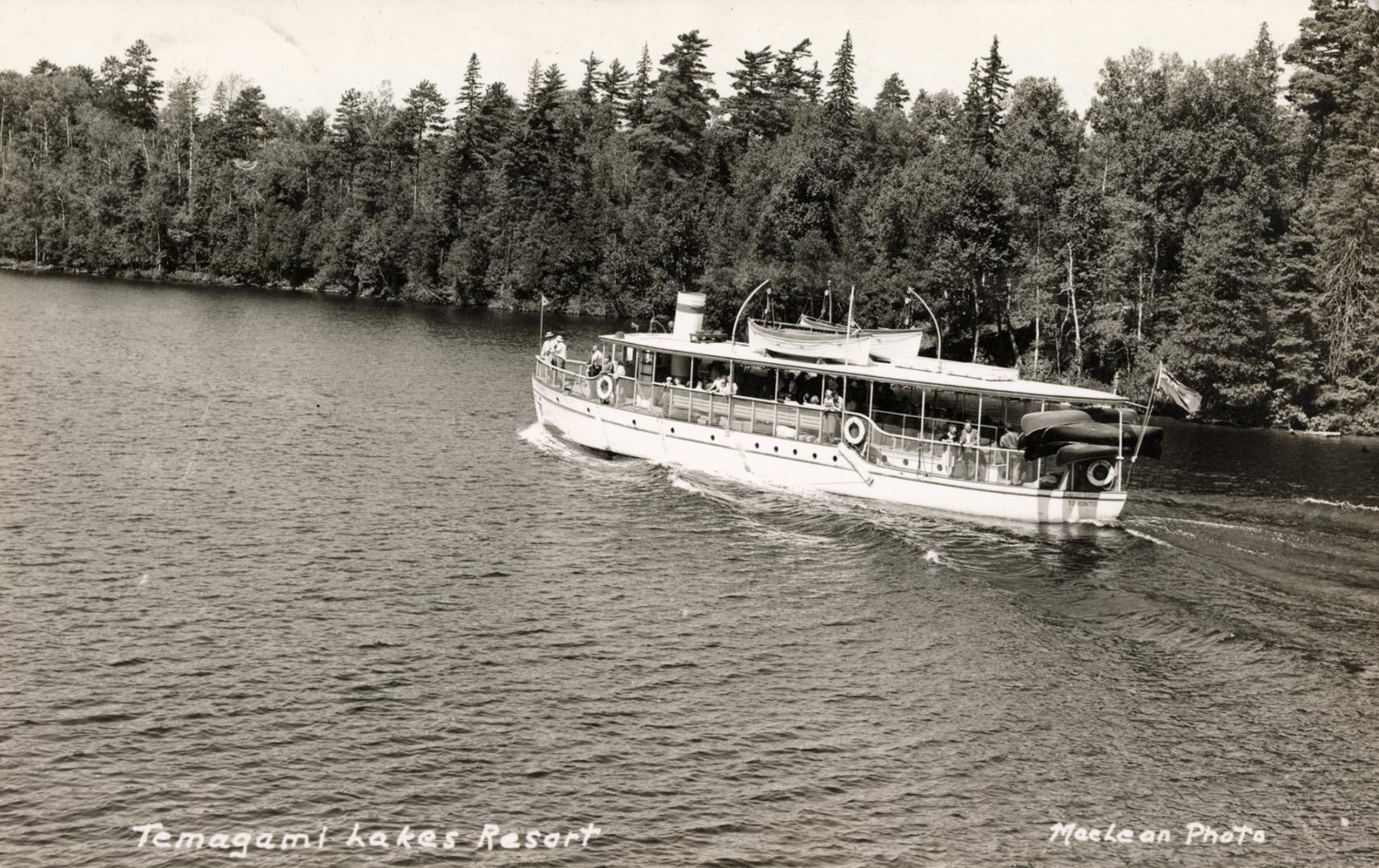 Black and white photograph of a lake in the wilderness with a steamboat cruising on it.