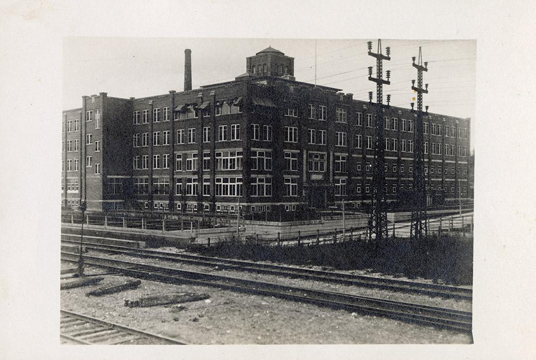 Black and white photograph of a four story hospital building with railway tracks in the foregro…