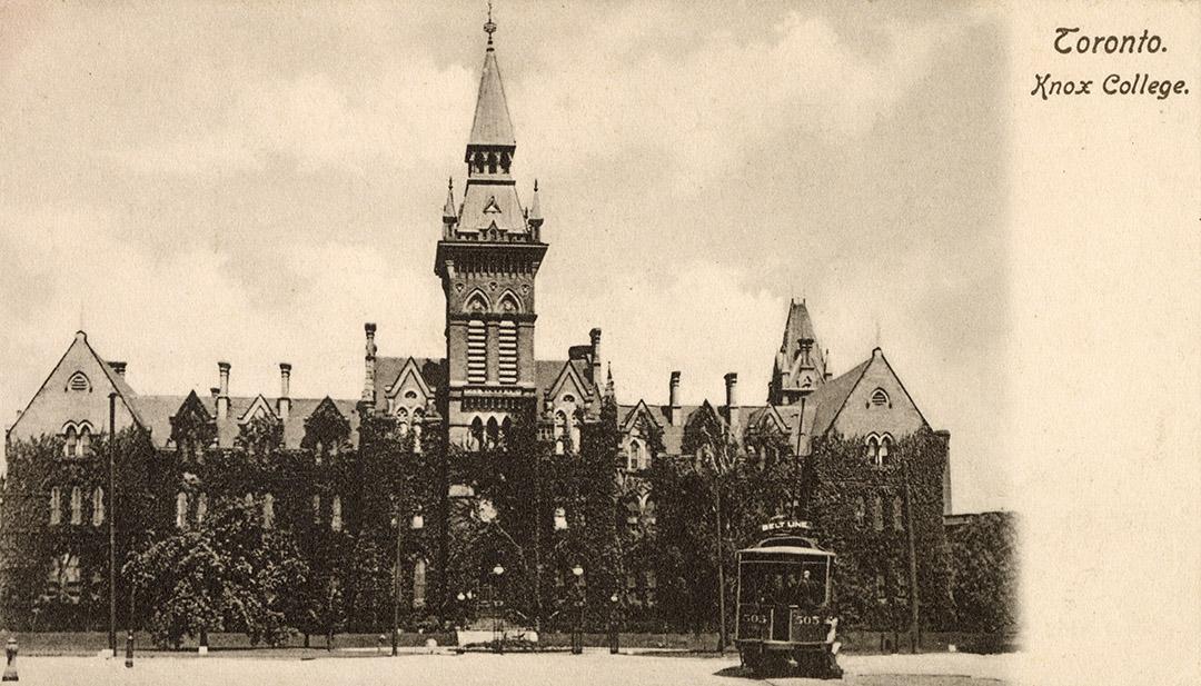 Black and white photograph of a gothic school building with a central tower. Streetcar in the f…