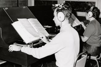 Two people listen to music and look at a score in a music library. 