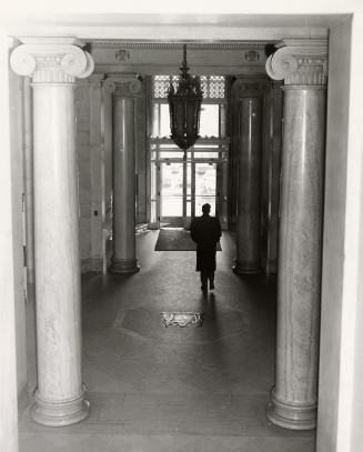 A photograph of a hallway in an office building, with a person walking away from the camera tow…