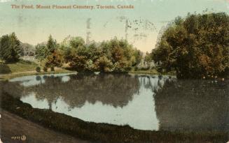 Colour postcard of a pond surrounded by trees. The caption on the top front states, "The Pond, …