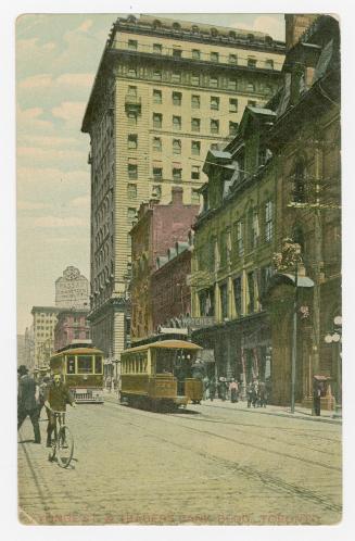 Colorized photograph of a busy downtown street in a city with a large skyscraper on the right h…