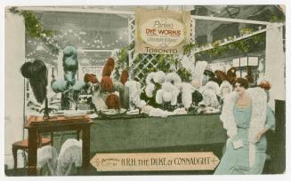 Colorized photograph of a woman standing in front of a shop counter full of dyed ostrich feathe…