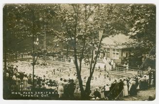 Black and white photograph of people swimming in a large pool in a wooded area.