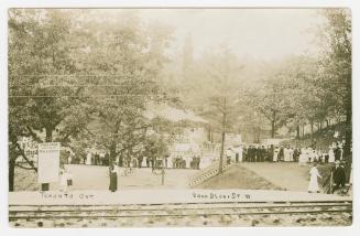 Black and white photograph of people walking towards large pool in a wooded area.