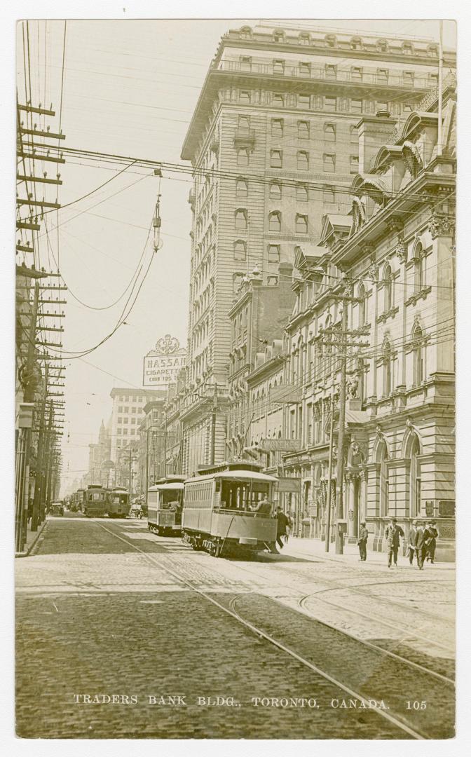 Black and white photograph of an early skyscraper in the right hand side of a busy city street.