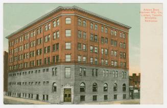 Picture of a large brick factory building on a street corner. 