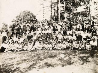 Photograph of a large group of people posed for a group photo in a park with trees in the backg…