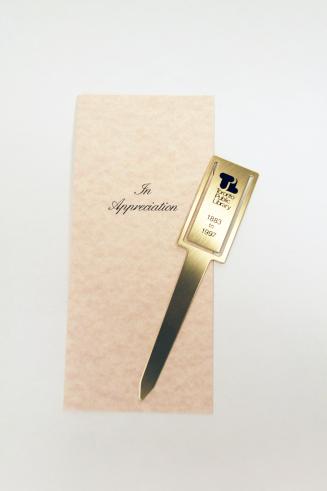 A brass letter opener with the old Toronto Public Library logo printed on it, inserted into a p…