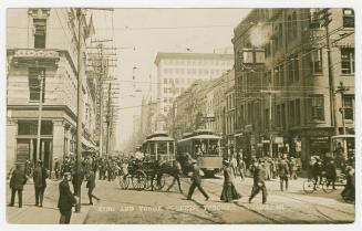 Black and white photograph of a busy city intersection with people, streetcars and horse drawn …